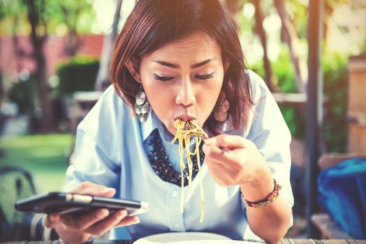 Asian women are happy when eating and playing mobile games,focus on the face.