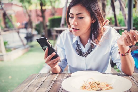 Asian women are happy when eating and playing mobile games,focus on the face.