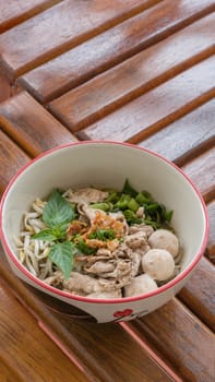 Asian white noodles with pork and vegetables in bowl over wooden background