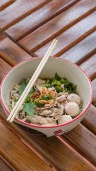 Asian white noodles with pork and vegetables in bowl over wooden background
