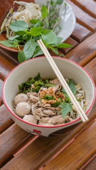 Asian white noodles with pork and vegetables in bowl over wooden background