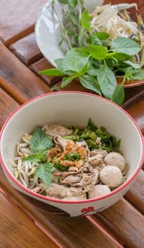 Asian white noodles with pork and vegetables in bowl over wooden background