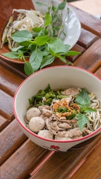 Asian white noodles with pork and vegetables in bowl over wooden background