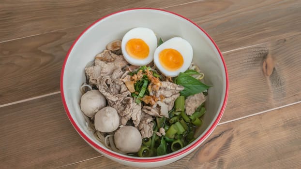 Asian white noodles with pork and vegetables in bowl over wooden background
