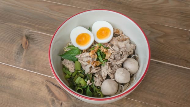 Asian white noodles with pork and vegetables in bowl over wooden background