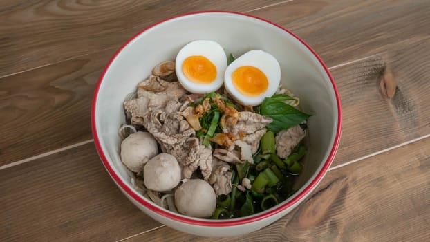Asian white noodles with pork and vegetables in bowl over wooden background