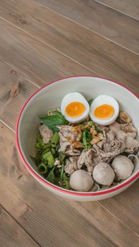 Asian white noodles with pork and vegetables in bowl over wooden background