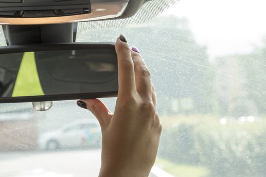 the girl in the cabin of the car  adjusts the rear view mirror