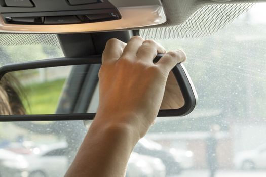 in the car the girl adjusts the rear view mirror