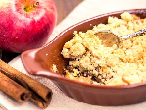 Homemade apple cramble cake with fresh apples and cinnamon sticks on rustic dark wooden background