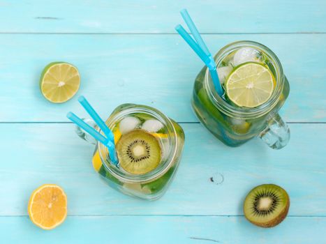 Cold homemade lemonade with fresh lemon, lime, kiwi and mint in mason jar. Summer drink on soft blue wooden background. Flat lay or top view