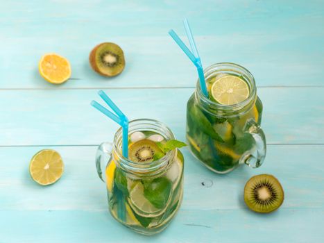 Cold homemade lemonade with fresh lemon, lime, kiwi and mint in mason jar. Summer drink on soft blue wooden background