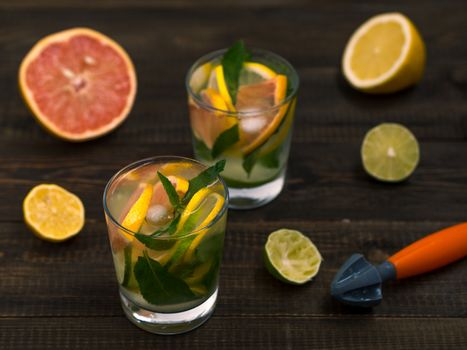 Cold homemade lemonade with fresh lemon, lime, grapefruit and mint by lemon reamer. Summer drink on dark wooden background