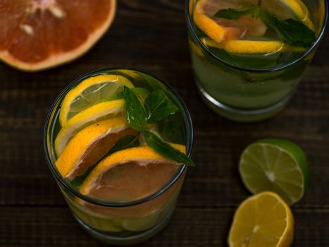 Closeup cold homemade lemonade with fresh lemon, lime, grapefruit and mint. Summer drink on dark wooden background