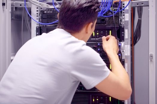 Young engeneer man in network server room connecting wires