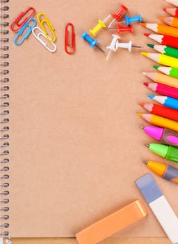 Notebook closeup with colored pencils, erasers, paperclips and buttons