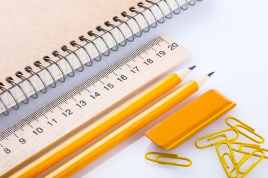 notebook, eraser, ruler, pencil and paperclips on white background