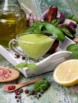 Freshly Made Creamy Pesto Sauce in Glass Gravy Boat with Raw Fresh Ingredients in White Wooden Tray closeup Cracked Wooden background