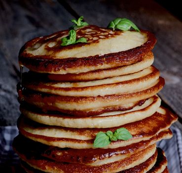 Stack of Delicious Homemade  Pancakes with Glazed Honey and Mint Leafs in Shadow closeup on Wooden background 