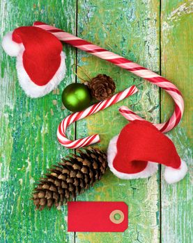Christmas Decoration Concept with Small Santa Hats, Striped Sweet Cane, Fir Cones and Greeting Card closeup on Rustic Cracked background