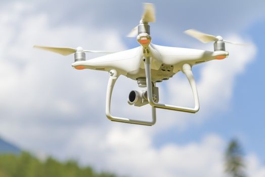 White drone quad copter with high resolution digital camera flying in the blue sky over the mountain