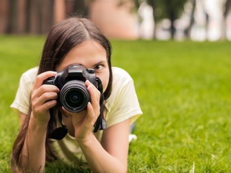 Young woman photographer with camera lie down on grass with copyspace
