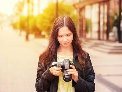 Cheerful young woman tourist watching shots in her dslr camera outdoors. Image with sunkissed effect. Vacation photography travel concept