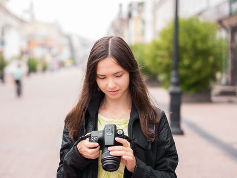 Cheerful young woman tourist watching shots in her dslr camera outdoors. Vacation photography travel concept