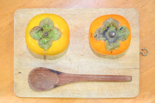 Two persimmon and Wood Spoon on the chopping block