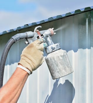 Spraying white paint onto a galvanized surface by an airbrush gun.