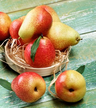 Ripe Yellow and Red Pears with Leafs in Wicker Bowl closeup on Green Wooden background