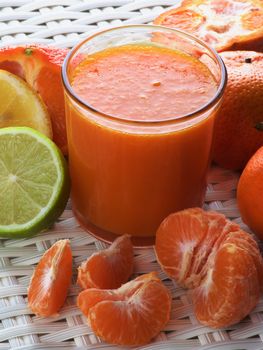 Freshly Squeezed Mixed Citrus Juice in Glass with Tangerines and Slices of Limes and Lemons closeup on Wicker background