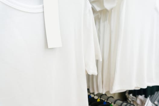 blank price tag hang over white tshirt on Hanger Shelf in Supermarket or Hypermarket Retail Store Outlet, Shallow Depth of Field.