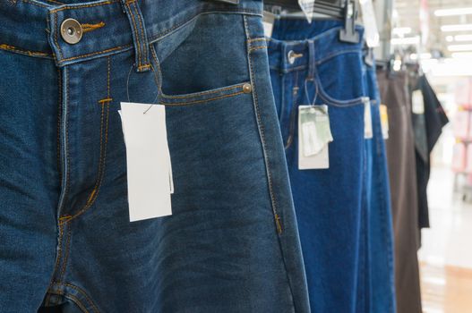 Blank White Tag over the Blue Jeans on Hanger Shelf in Supermarket or Hypermarket Retail Outlet Store, Shallow Depth of Field
