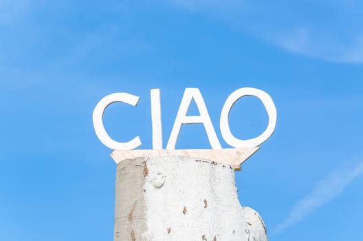 Ciao lettering on an old tree trunk in front of blue sky.