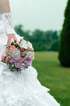 wedding bouquet in hands of the bride with roses, orchids and ribbons