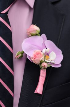 a boutonniere of roses and orchids on a blue jacket of the groom