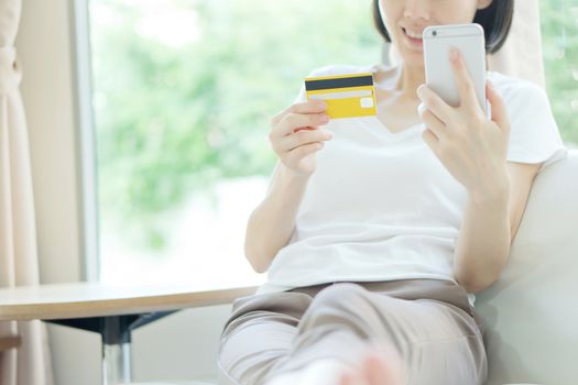 Woman shopping on tablet computer and credit card sitting in sofa smiling happy.