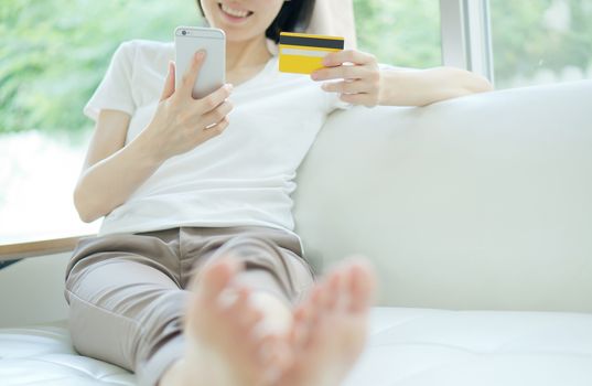 Woman shopping on tablet computer and credit card sitting in sofa smiling happy.