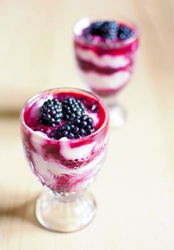 Glass cups with cream cheese blackberry desserts. Fresh blackberries are placed on top of the desserts.