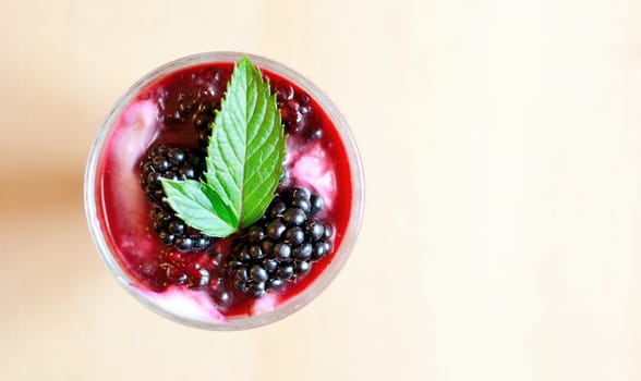 Top view on glass cup with cream cheese blackberry dessert. Fresh blackberries and mint leaves are placed on top of the desserts.