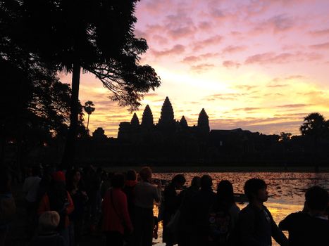 Many Asian tourists taking picture of ancient temple Angkor Wat at sunrise. Siem Reap, Cambodia. Towers of Angkor Wat reflected in lake at dawn. Angkor Wat is a popular tourist attraction.