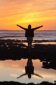 Silhouette of free woman enjoying freedom feeling happy at beach at sunset. Serene relaxing woman in pure happiness and elated enjoyment with arms raised outstretched up. 