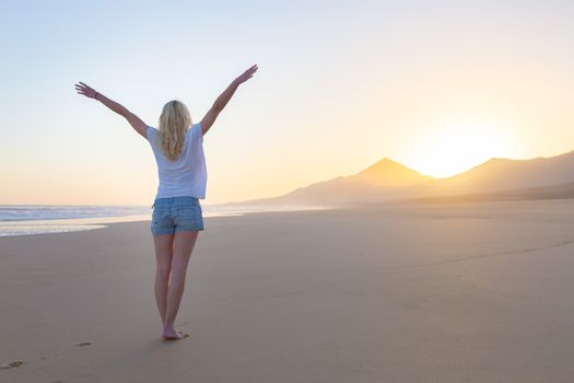 Free woman enjoying freedom feeling happy at beach at sunrise. Serene relaxing woman in pure happiness and elated enjoyment with arms raised outstretched up. 