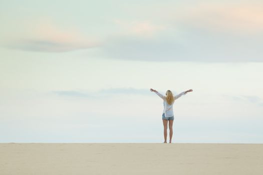 Woman enjoying freedom feeling as a bird at beach at dusk. Serene relaxing woman in pure happiness and elated enjoyment with arms raised outstretched up. 