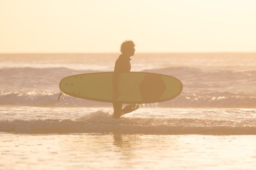 Male surfer on the beach with the surfboard in sunset. Vertical composition.