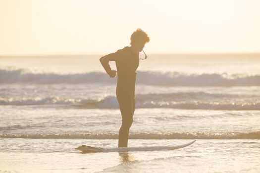 Male surfer on the beach with the surfboard in sunset.  Vertical composition.