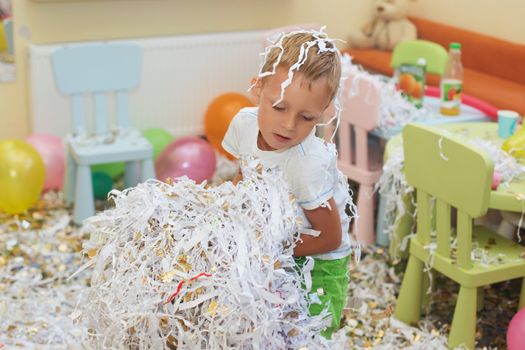 Little boy jumping and having fun celebrating birthday. Portrait of a child throws up multi-colored tinsel and paper confetti. Kids party. Happy excited laughing kid under sparkling confetti shower