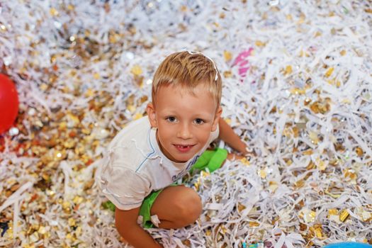 Little boy jumping and having fun celebrating birthday. Portrait of a child throws up multi-colored tinsel and paper confetti. Kids party. Happy excited laughing kid under sparkling confetti shower