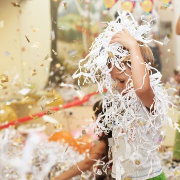 Little boy jumping and having fun celebrating birthday. Portrait of a child throws up multi-colored tinsel and paper confetti. Kids party. Happy excited laughing kid under sparkling confetti shower